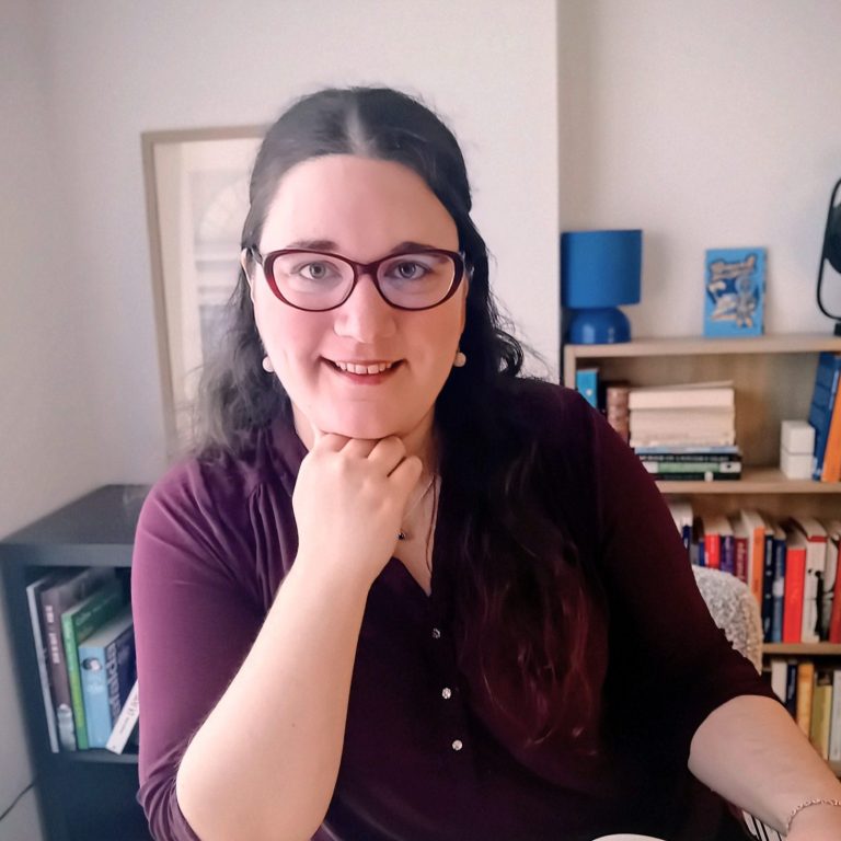 Marion at her desk, smiling, with a bookshelf behind her